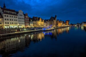 Vista notturna del lungofiume della Motława a Danzica con riflessi sull’acqua e centro storico illuminato