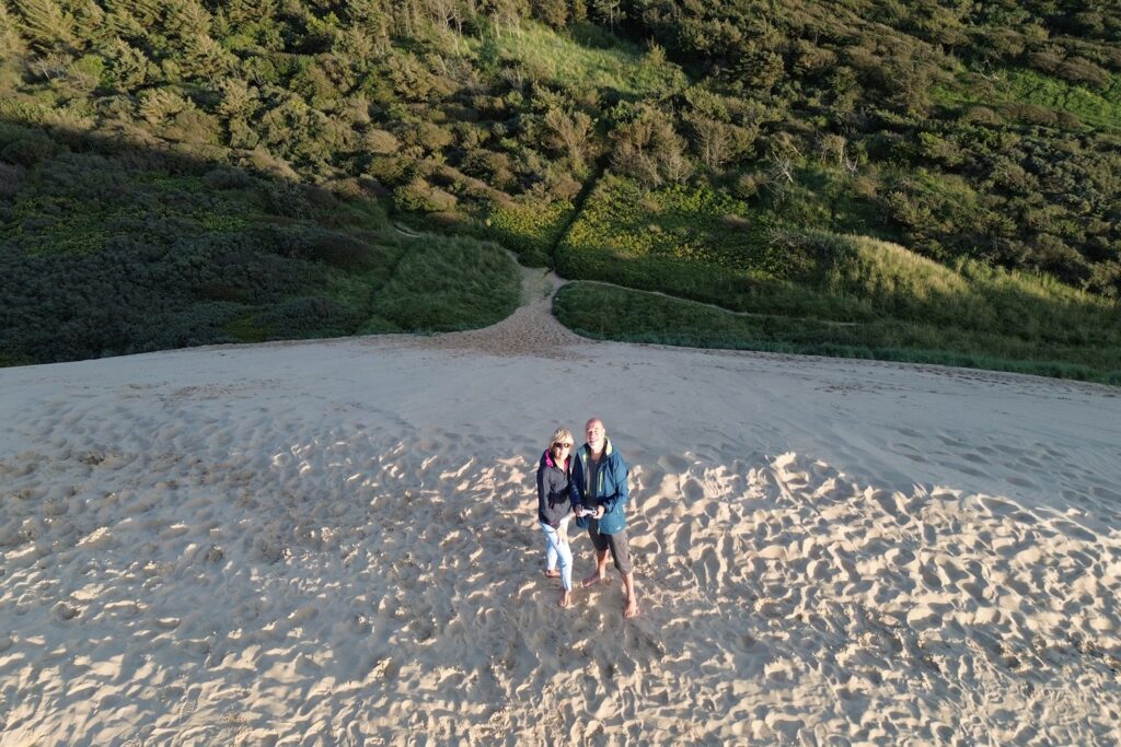 Danimarca on the Road: il viaggio che non ti aspetti 11 Due viaggiatori sulla sommità della duna di Rubjerg Knude, in Danimarca, dopo la salita attraverso la sabbia, con la vegetazione costiera sullo sfondo.