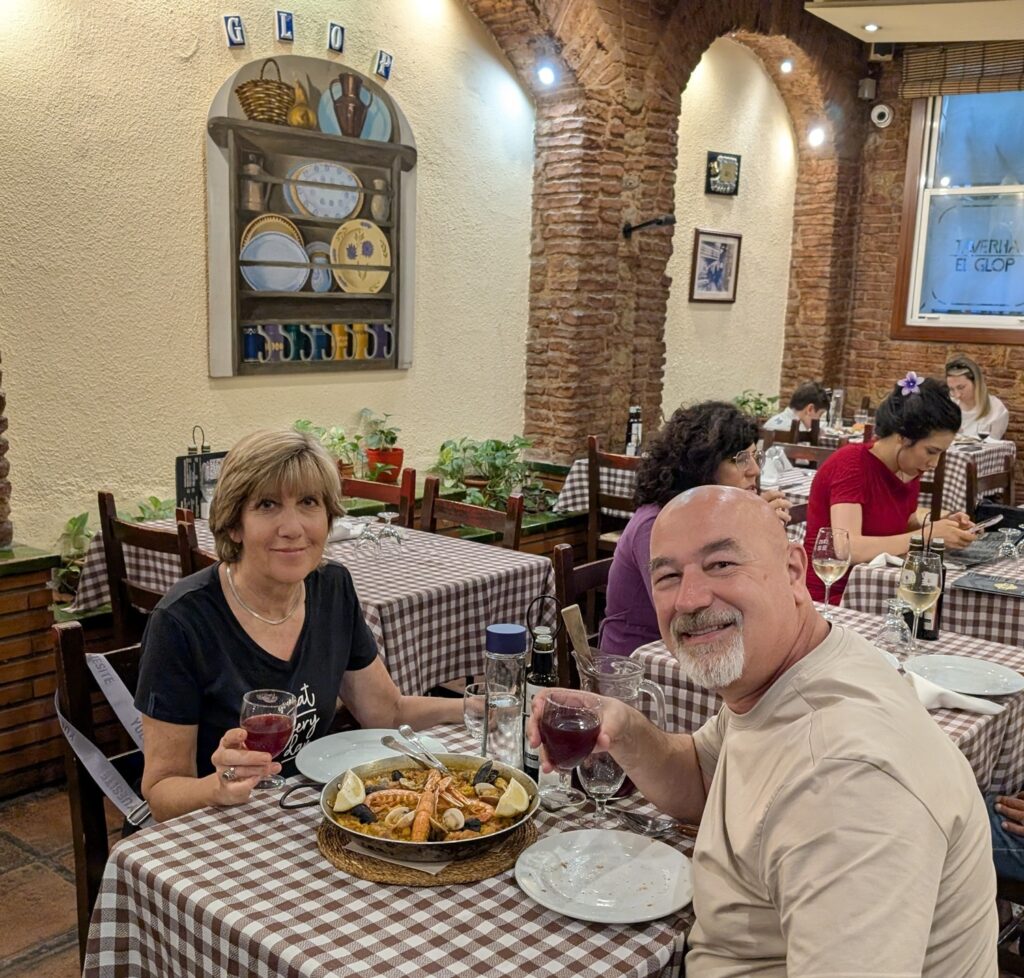 Barcellona in 6 giorni: molto più della città di Gaudí 34 Due viaggiatori brindano davanti a una paella in una tradizionale taverna di Barcellona durante una cena tipica catalana.