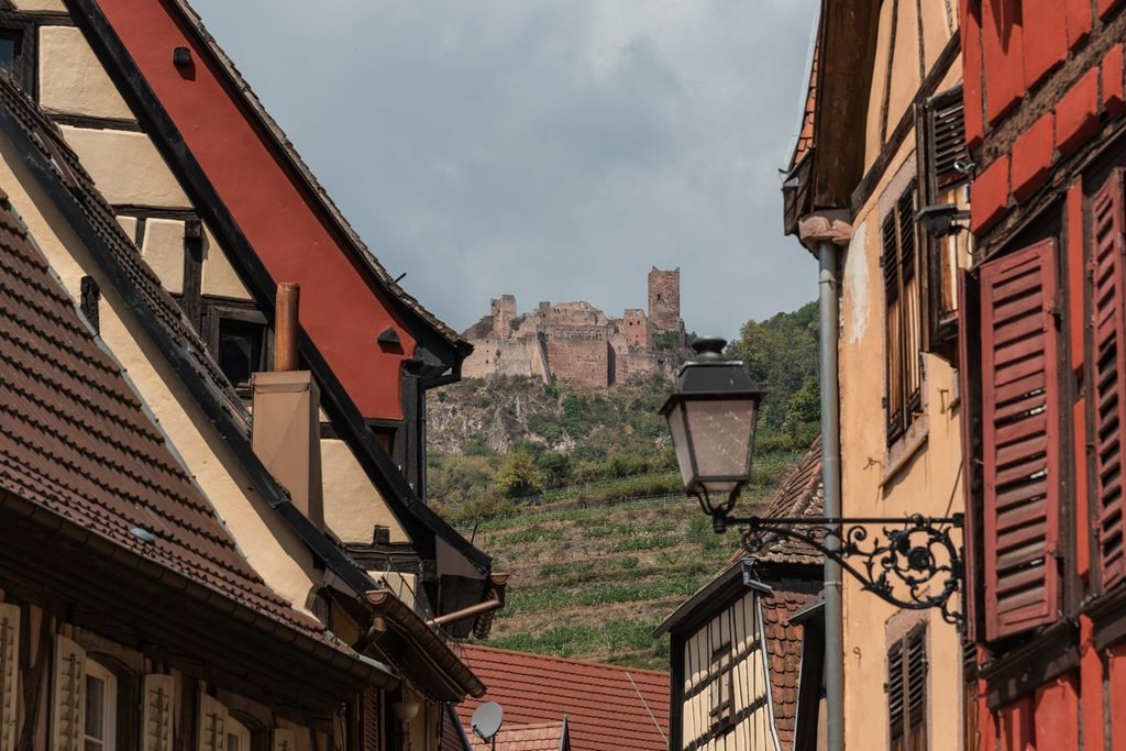 9 giorni in Alsazia 5 Scorcio di Ribeauvillé in Alsazia con le case tradizionali e le rovine di un castello medievale sulla collina.